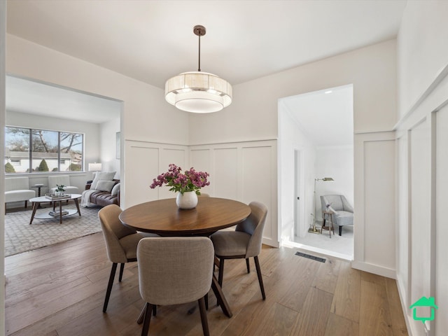 dining area featuring visible vents, a decorative wall, hardwood / wood-style floors, and a wainscoted wall