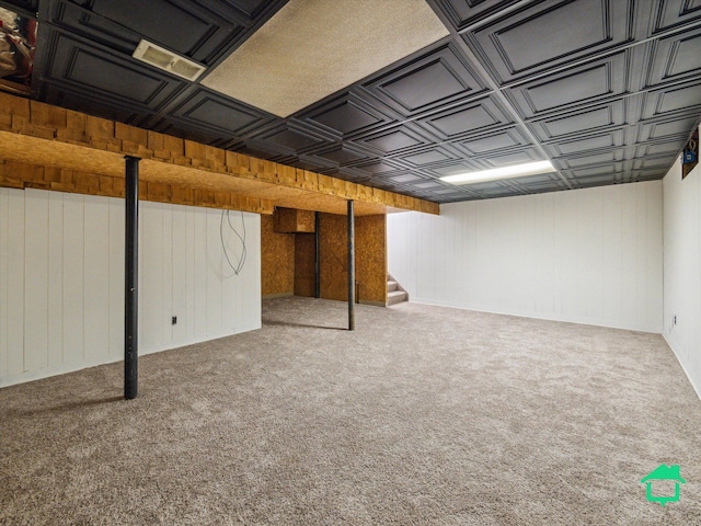 finished below grade area featuring an ornate ceiling, wooden walls, carpet flooring, and stairs