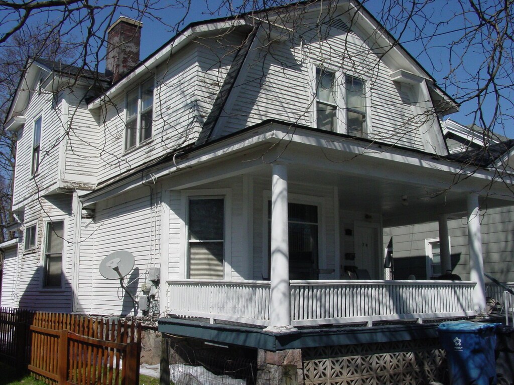 view of side of home with a gambrel roof, a porch, a chimney, and fence