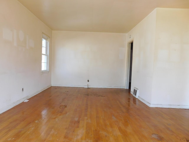 spare room featuring wood-type flooring, visible vents, and baseboards
