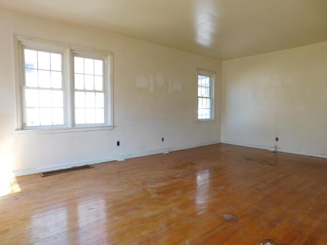 unfurnished room featuring wood-type flooring, visible vents, and baseboards
