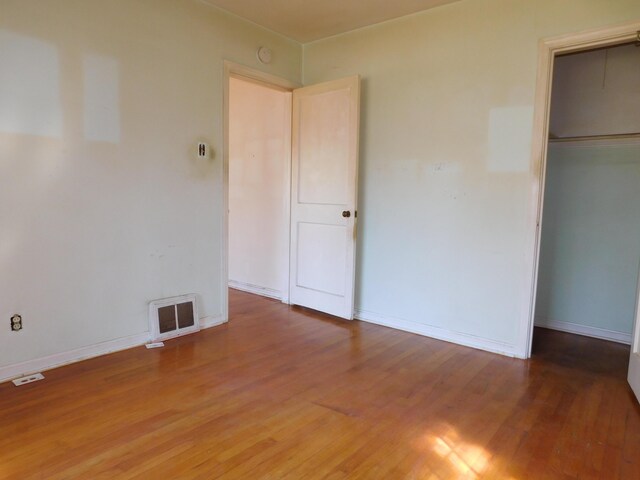 unfurnished bedroom featuring baseboards, wood finished floors, visible vents, and a closet