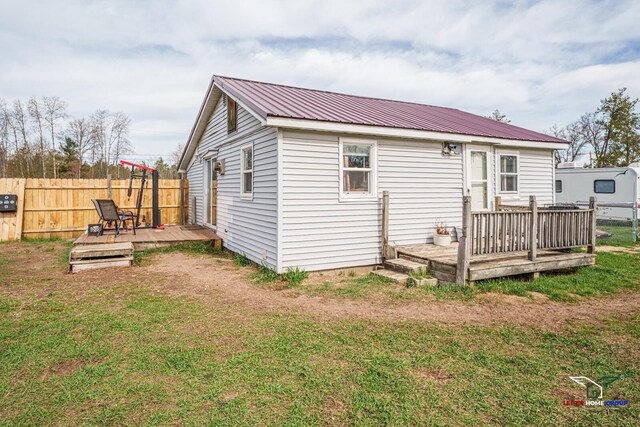 back of property featuring fence, a wooden deck, a yard, and metal roof