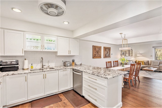 kitchen with stainless steel dishwasher, a sink, a peninsula, tasteful backsplash, and white cabinetry