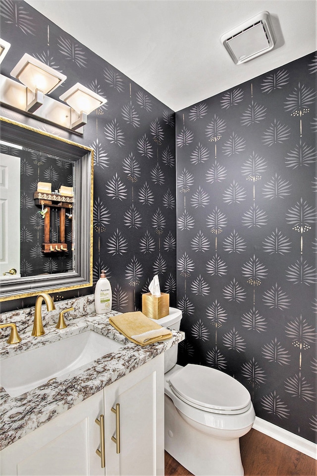 half bathroom featuring toilet, baseboards, wallpapered walls, wood finished floors, and vanity