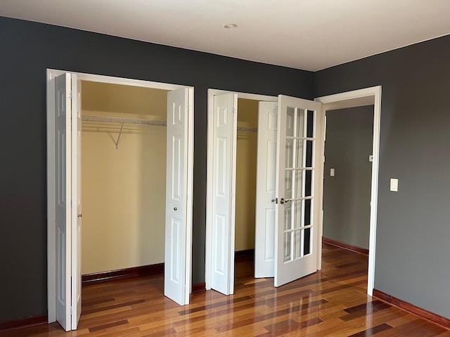 unfurnished bedroom featuring baseboards, wood finished floors, and multiple closets