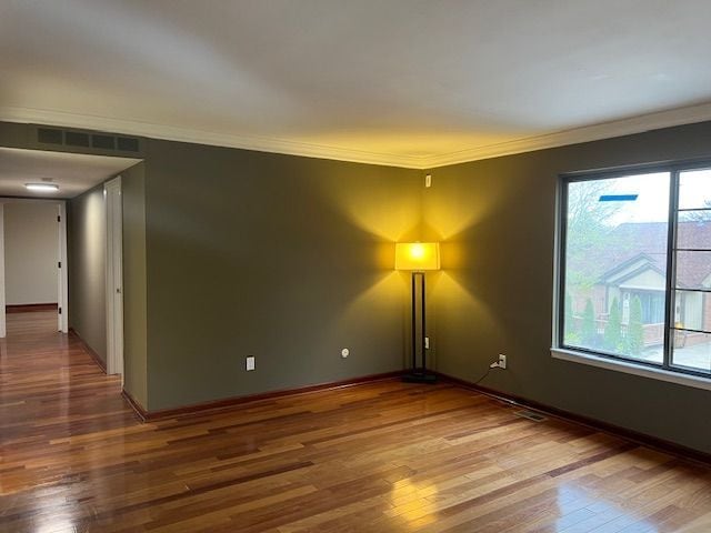 spare room with wood finished floors, plenty of natural light, visible vents, and crown molding