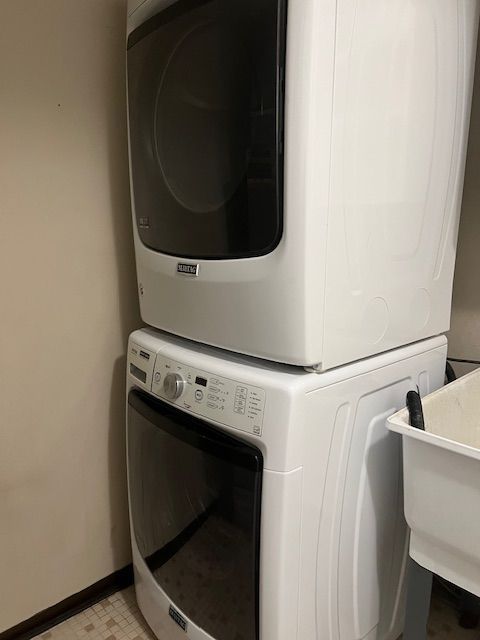 clothes washing area with stacked washer and clothes dryer, laundry area, and baseboards