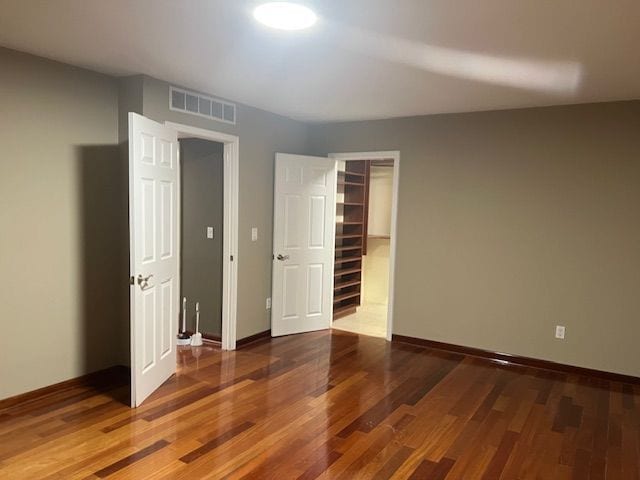 unfurnished bedroom featuring wood finished floors, visible vents, a closet, and baseboards