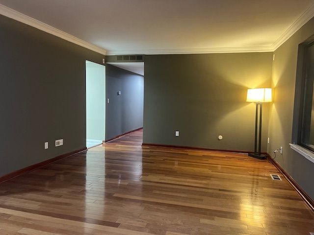 unfurnished room with crown molding, visible vents, and wood finished floors