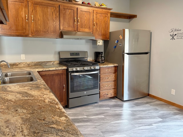kitchen featuring brown cabinets, a sink, under cabinet range hood, baseboards, and appliances with stainless steel finishes