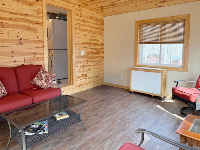 living room with wood ceiling, wood walls, baseboards, stacked washing maching and dryer, and wood finished floors