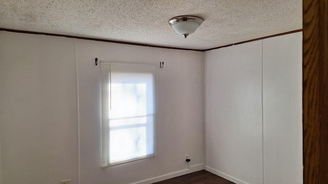 empty room with dark wood finished floors, a textured ceiling, and crown molding
