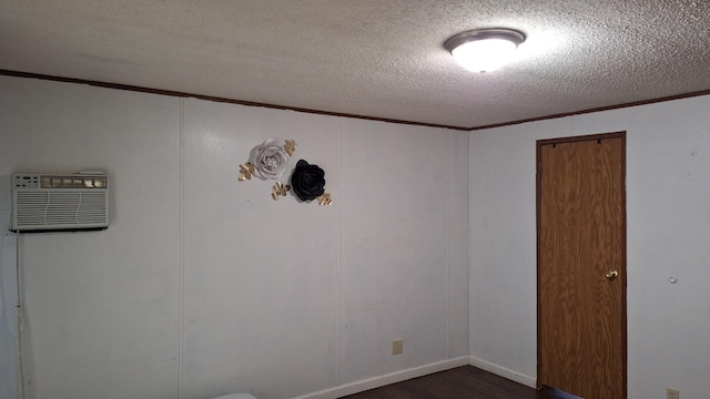 empty room with dark wood finished floors, a wall mounted AC, a textured ceiling, and crown molding