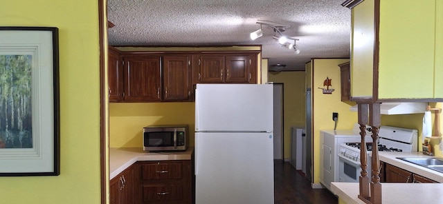 kitchen with light countertops, rail lighting, white appliances, a textured ceiling, and dark wood-style flooring