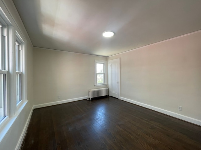 spare room featuring baseboards, radiator heating unit, and dark wood-type flooring