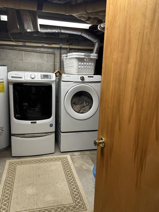 clothes washing area featuring concrete block wall, washing machine and dryer, water heater, and laundry area