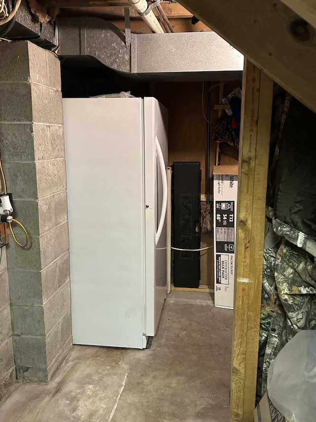 below grade area featuring freestanding refrigerator and concrete block wall