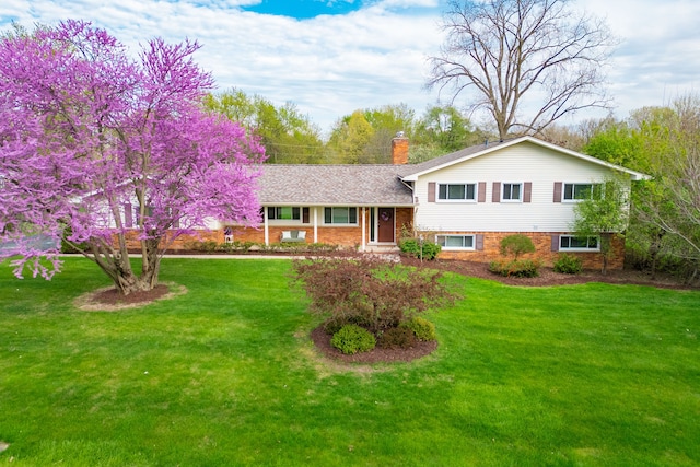 split level home with brick siding, a chimney, and a front yard