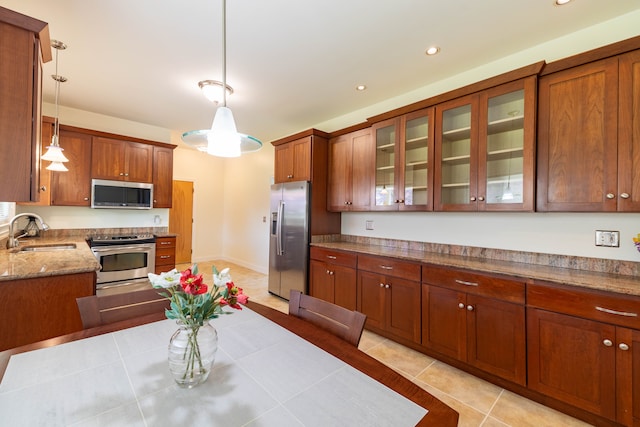kitchen featuring decorative light fixtures, appliances with stainless steel finishes, brown cabinets, a sink, and glass insert cabinets