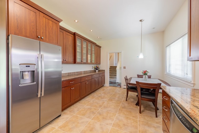 kitchen with brown cabinetry, appliances with stainless steel finishes, light tile patterned floors, light stone counters, and glass insert cabinets