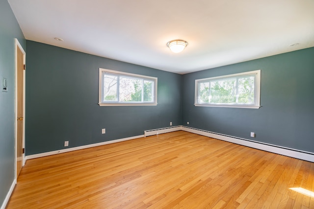 empty room featuring baseboards, a baseboard heating unit, and light wood finished floors