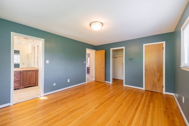 unfurnished bedroom featuring baseboards, a sink, ensuite bathroom, and light wood-type flooring