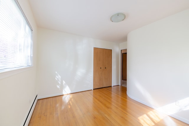 spare room featuring baseboards, a baseboard heating unit, and light wood-type flooring