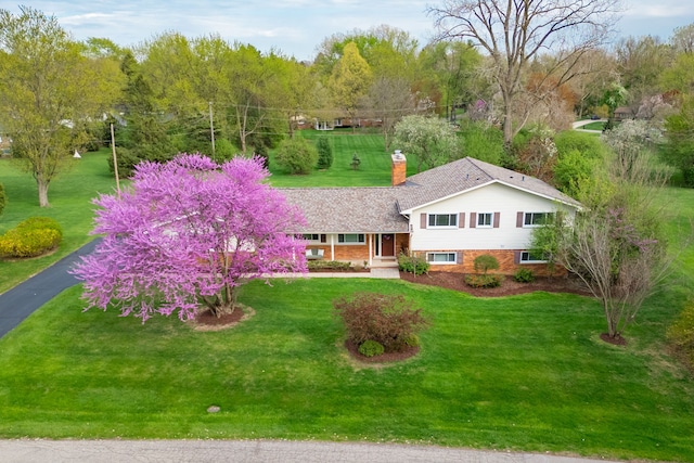 split level home featuring a chimney, a front yard, and brick siding