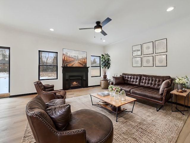 living room featuring recessed lighting, a ceiling fan, light wood-style floors, and a warm lit fireplace
