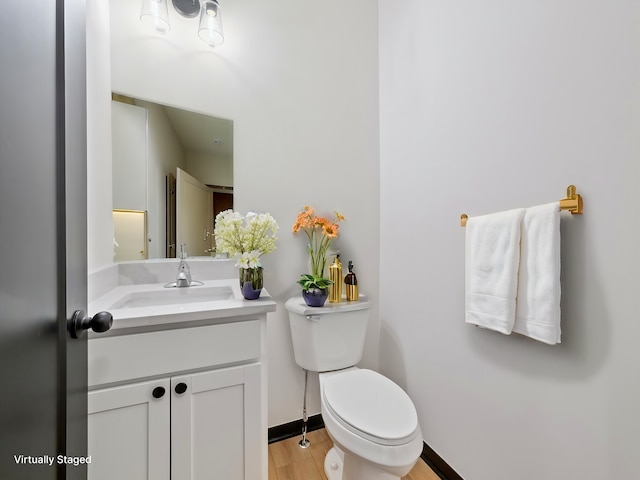 bathroom with toilet, wood finished floors, vanity, and baseboards