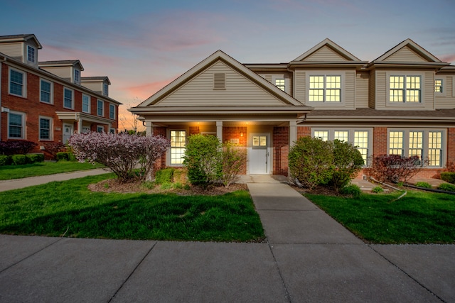 townhome / multi-family property featuring brick siding, a front lawn, and covered porch
