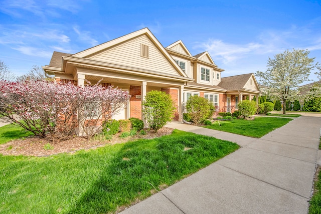 view of front of home featuring covered porch, a front yard, and brick siding