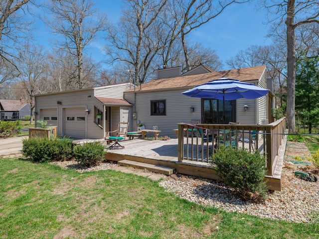 back of property featuring roof with shingles, a garage, a deck, a chimney, and a lawn