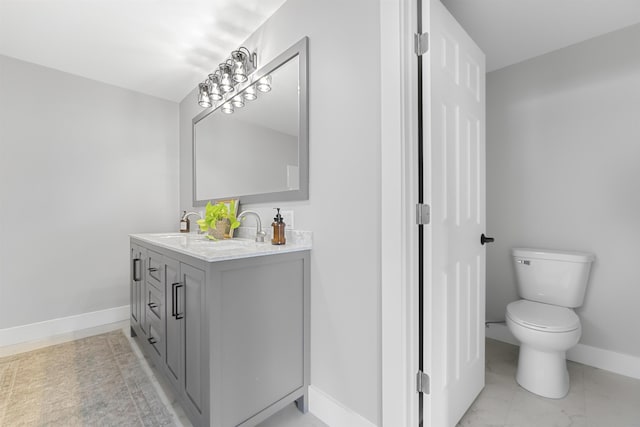 full bath with a sink, toilet, marble finish floor, double vanity, and baseboards