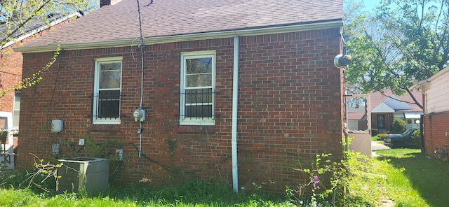 view of side of home with brick siding, cooling unit, a shingled roof, and a chimney
