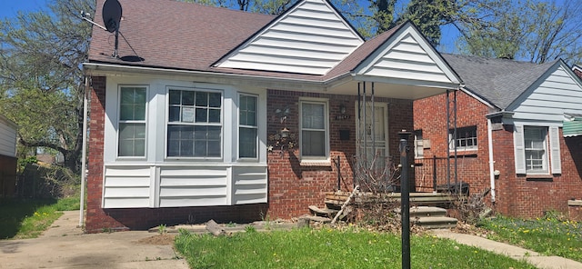 bungalow-style home featuring roof with shingles and brick siding