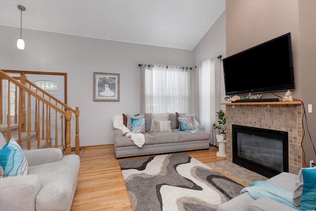 living room with wood finished floors, vaulted ceiling, a fireplace with flush hearth, stairway, and baseboards