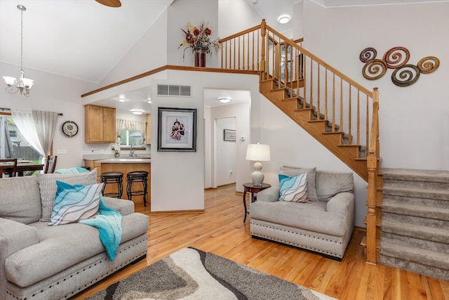 living area with a chandelier, high vaulted ceiling, light wood-type flooring, stairway, and baseboards
