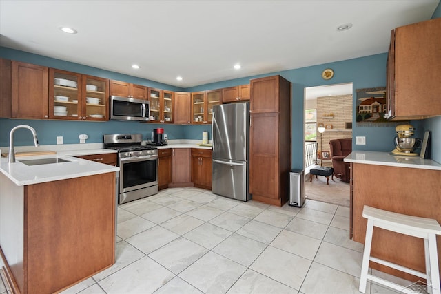 kitchen with a sink, glass insert cabinets, brown cabinetry, light countertops, and appliances with stainless steel finishes