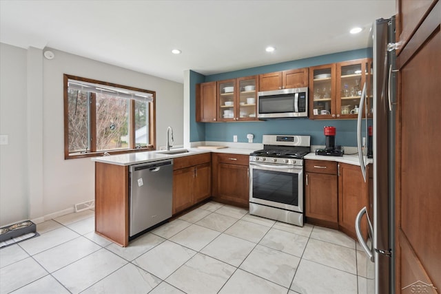 kitchen featuring brown cabinets, a peninsula, appliances with stainless steel finishes, and a sink