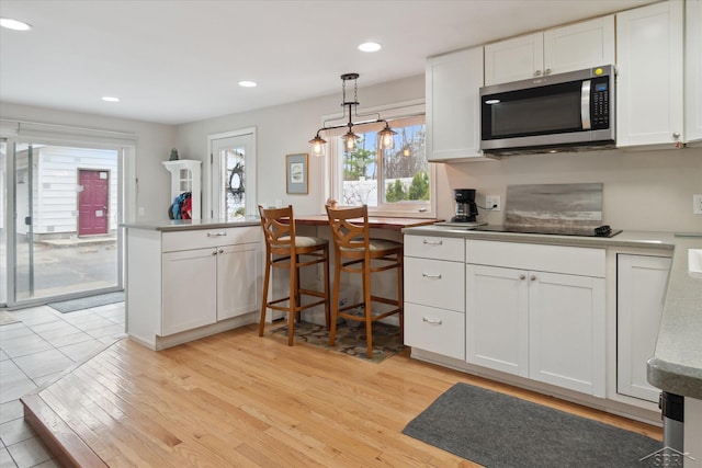 kitchen featuring stainless steel microwave, decorative light fixtures, black electric cooktop, white cabinets, and light wood finished floors