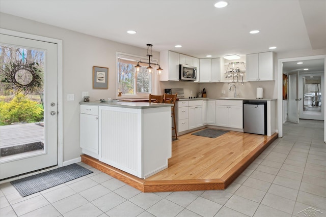kitchen featuring light tile patterned flooring, a peninsula, white cabinets, and appliances with stainless steel finishes
