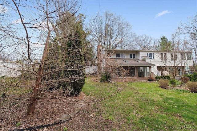 view of front facade featuring a chimney, a shingled roof, a front lawn, and a sunroom