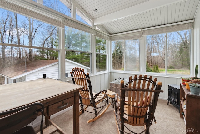 sunroom / solarium featuring lofted ceiling with beams and a wood stove