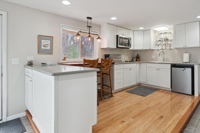 kitchen featuring a sink, stainless steel appliances, a peninsula, hanging light fixtures, and white cabinets