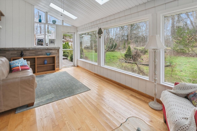 sunroom with wood finished floors, wooden walls, and vaulted ceiling with skylight