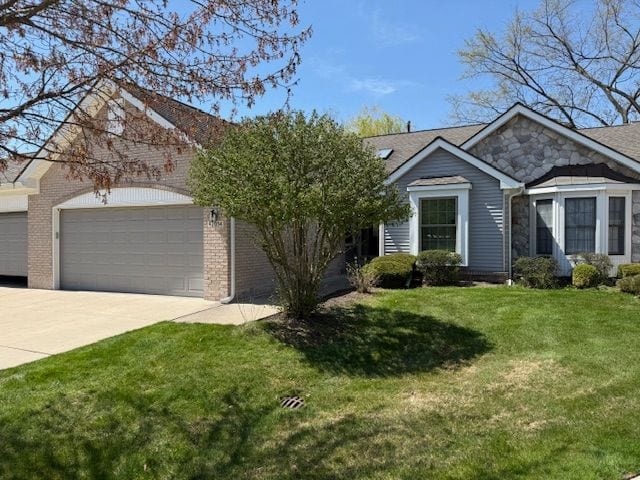 ranch-style home with a front lawn, stone siding, brick siding, concrete driveway, and an attached garage