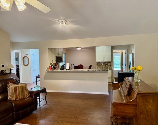 living room featuring dark wood-style flooring, ceiling fan, and baseboards