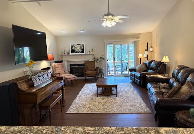 living room featuring wood finished floors, a ceiling fan, lofted ceiling, and a glass covered fireplace